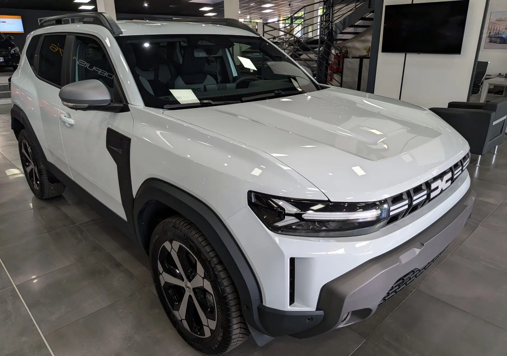 Vue 3/4 avant droite du Dacia Duster Hybrid-G blanc Glacier avec jantes bi-ton et protections noires contrastantes.