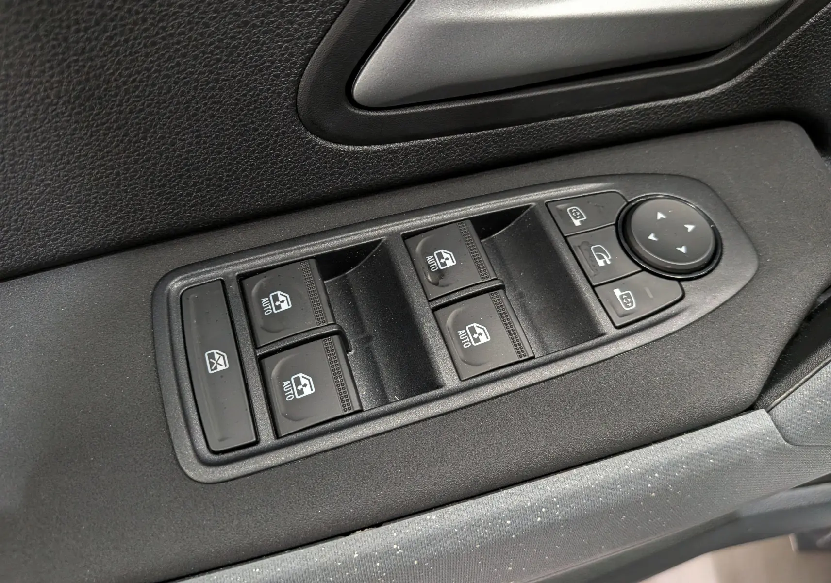 Gros plan sur les commandes de lève-vitres et rétroviseurs côté conducteur du Dacia Duster Hybrid-G 150 CH 4x4, intérieur noir.