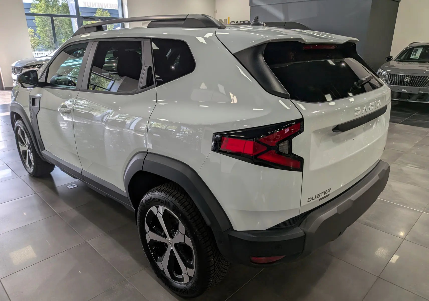 Vue 3/4 arrière droite du Dacia Duster Hybrid-G blanc Glacier, soulignant ses feux arrière et ses jantes bi-ton.