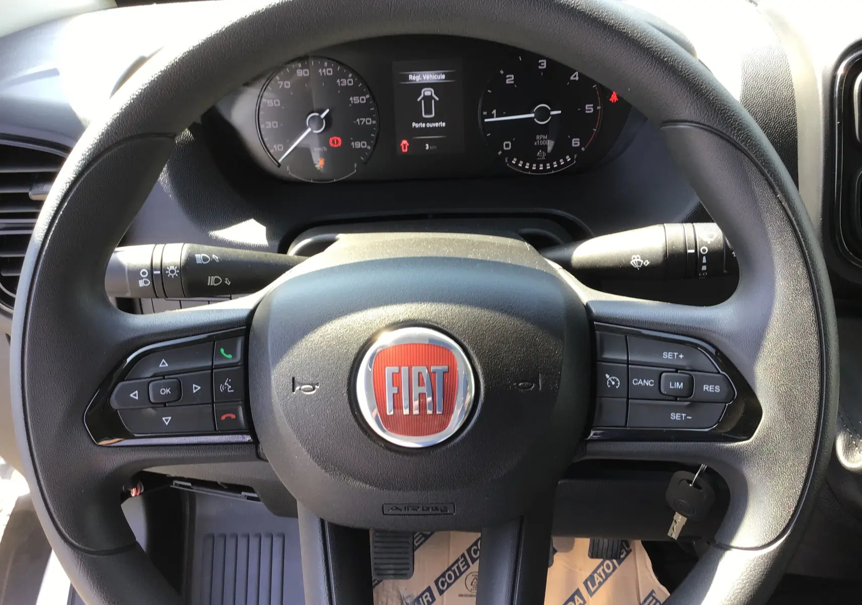 Volant noir du Fiat Ducato Chassis Benne 2023 avec commandes intégrées et tableau de bord visible en arrière-plan.