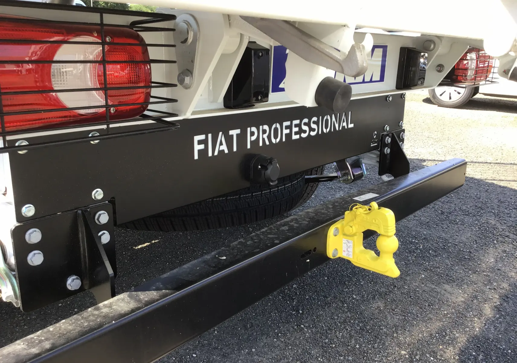 Gros plan arrière droit du FIAT Ducato Chassis Benne blanc avec attelage jaune et protection des feux.