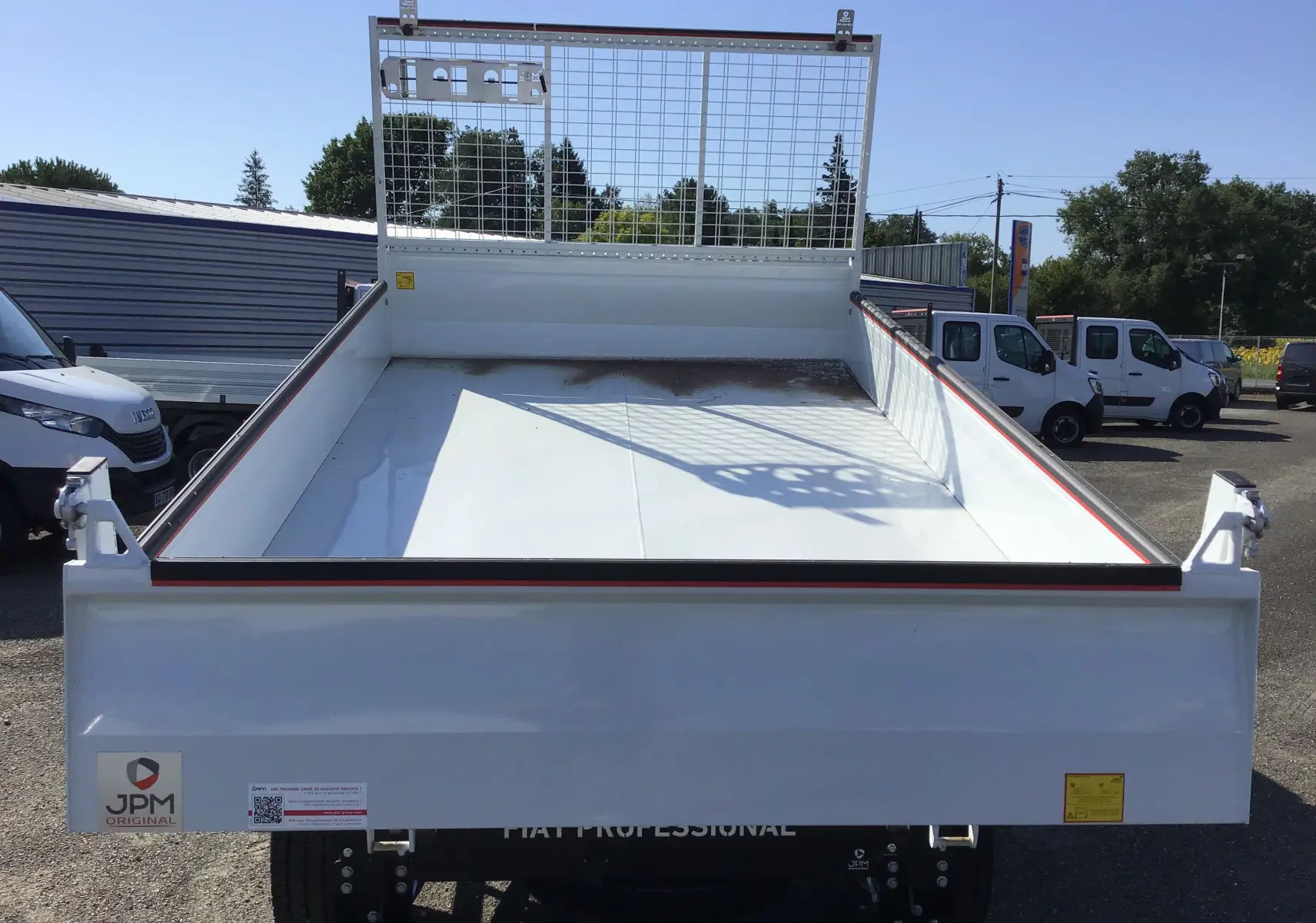 Vue arrière d'un FIAT Ducato Chassis Benne blanc 2023 avec benne acier et grille de protection métallique.