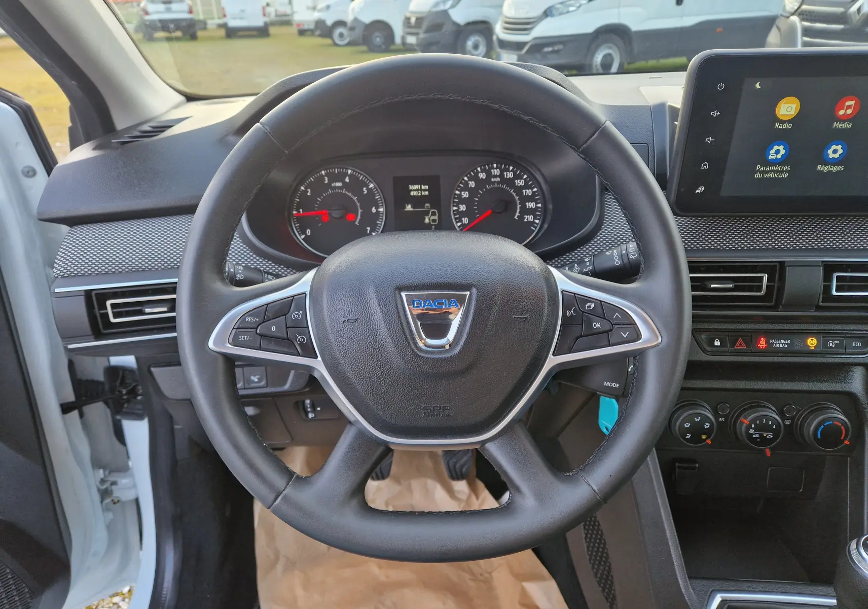 Vue intérieure centrée sur le volant noir du Dacia Sandero blanc 2022 avec tableau de bord et écran tactile visible.
