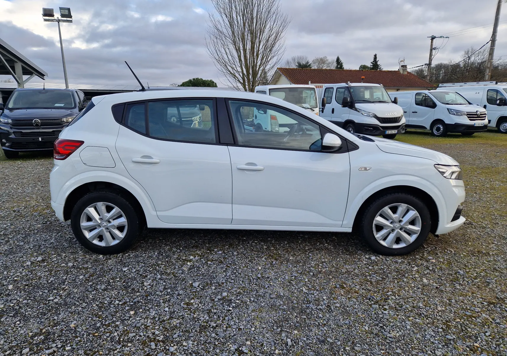 Vue de profil côté gauche d'une Dacia Sandero blanche 2022 bicarburation essence/GPL sur un parking extérieur.