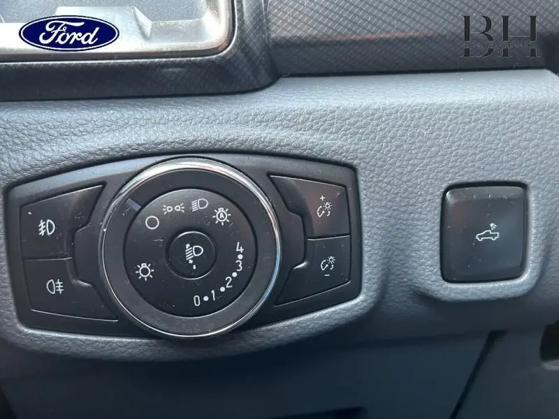 Gros plan sur les commandes d’éclairage et ouverture de coffre du Ford Ranger Wildtrak 2017, intérieur noir texturé.