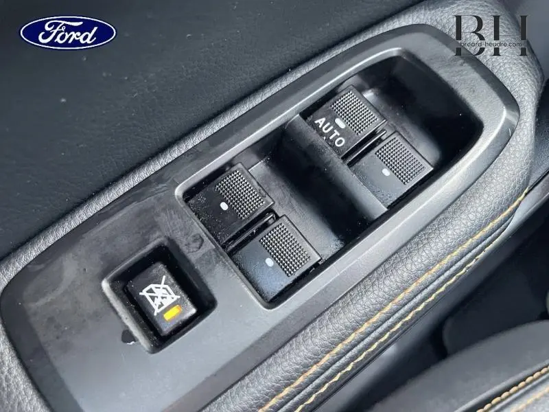 Gros plan sur les commandes des vitres électriques côté conducteur du Ford Ranger Wildtrak orange avec surpiqûres orange.