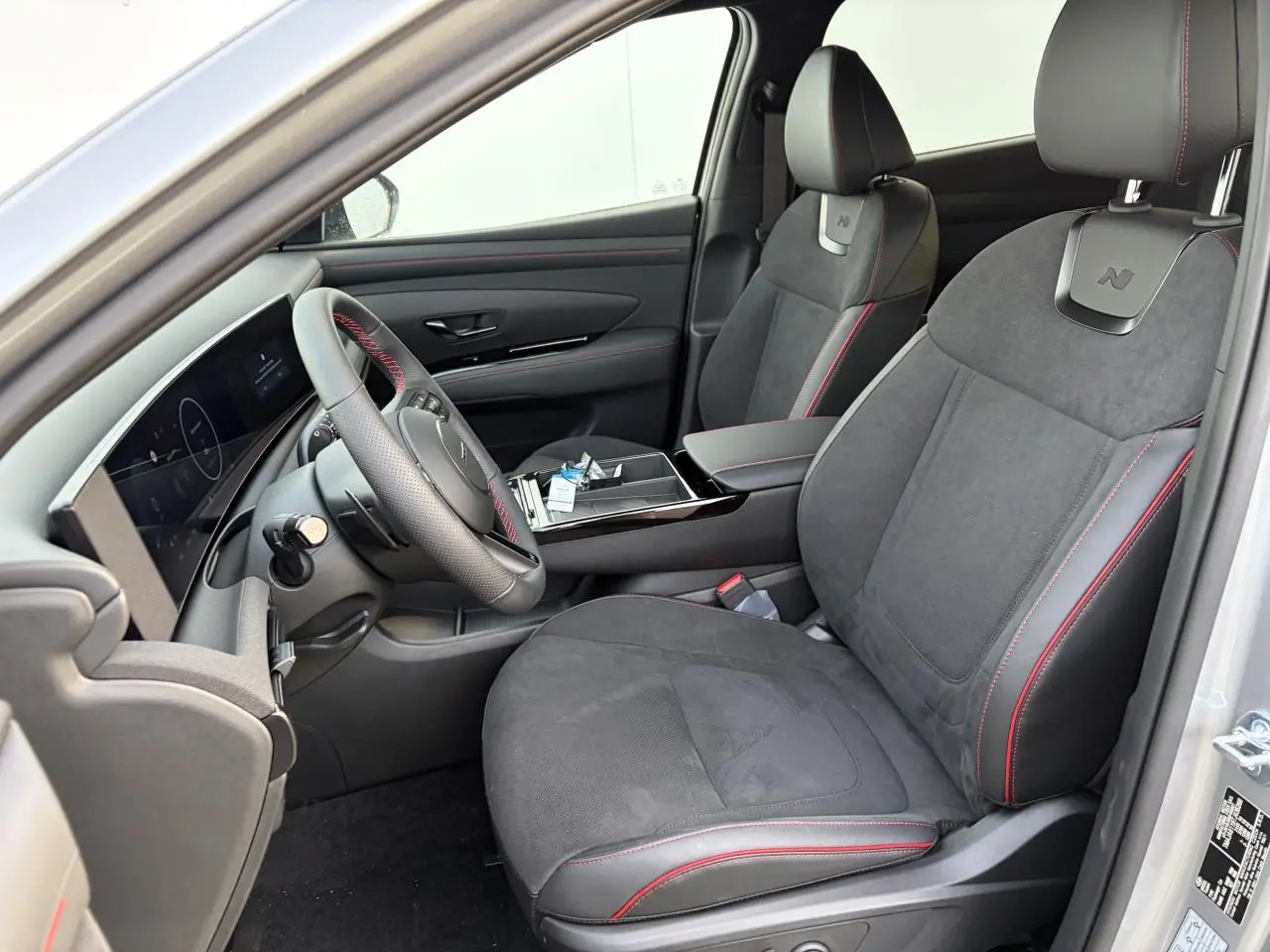 Vue intérieure côté conducteur du Hyundai Tucson 2025, sièges cuir/alcantara noirs avec surpiqûres rouges et volant sport N Line.
