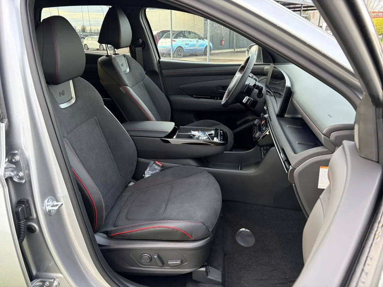 Vue intérieure côté conducteur du Hyundai Tucson 2025 argent métallisé avec sellerie N Line cuir/alcantara noire et surpiqûres rouges.