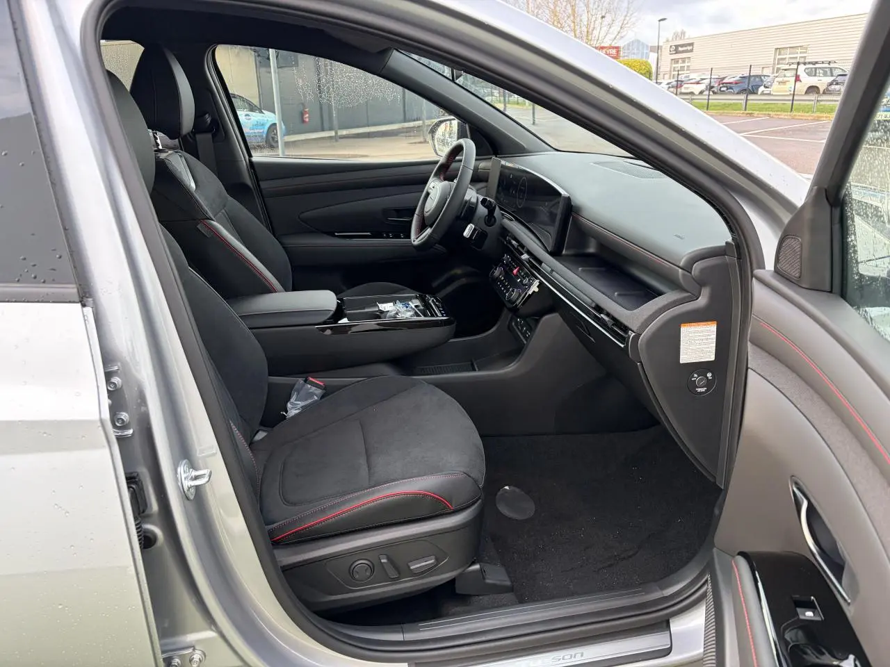 Vue intérieure côté conducteur du Hyundai Tucson 2025 en Shimmering Silver, sièges cuir/alcantara noirs avec surpiqûres rouges.
