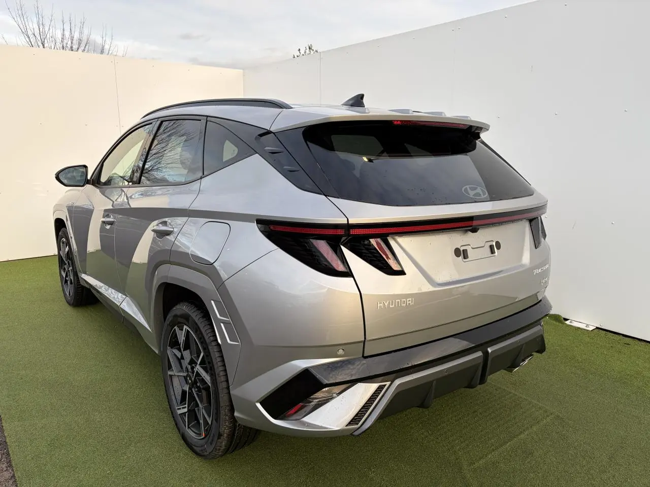 Vue 3/4 arrière gauche du Hyundai Tucson 2025 en gris métallisé avec feux arrière à LED et jantes alliage noires.