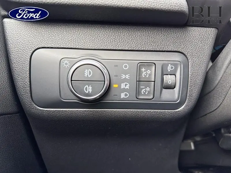 Gros plan sur les commandes d’éclairage du Ford Kuga 2022, tableau de bord noir texturé.