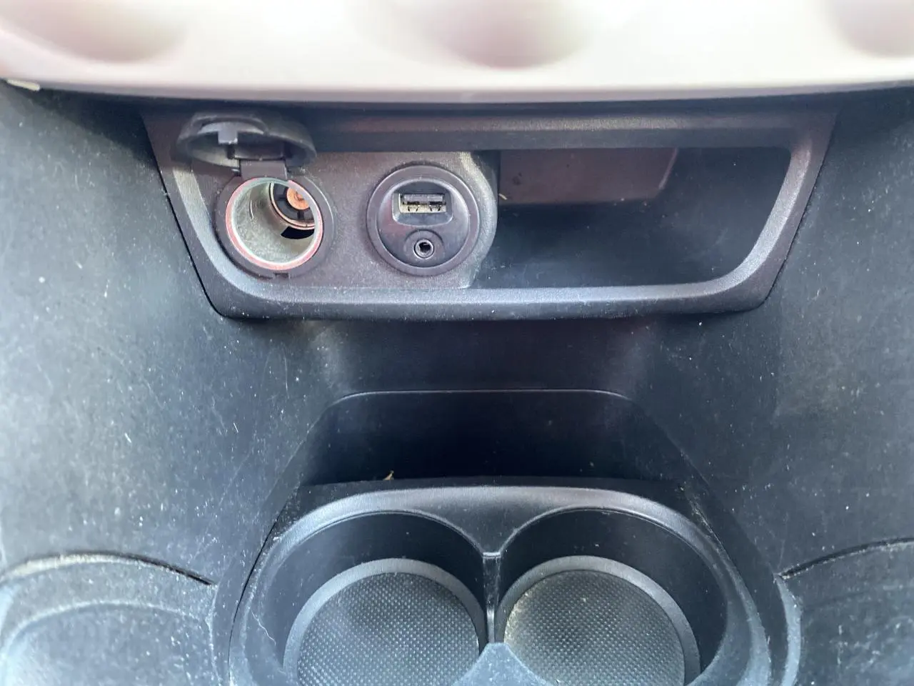 Prise 12V et port USB au-dessus des porte-gobelets noirs dans l’habitacle d’une Peugeot 208 gris foncé.