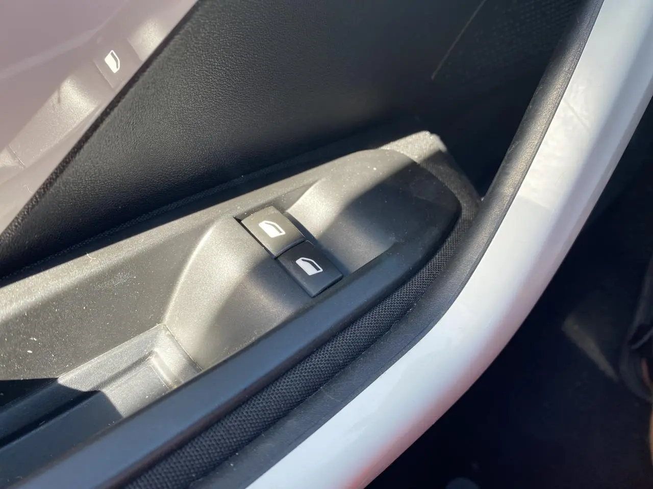 Gros plan sur les commandes des lève-vitres électriques côté conducteur d'une Peugeot 208 gris foncé.