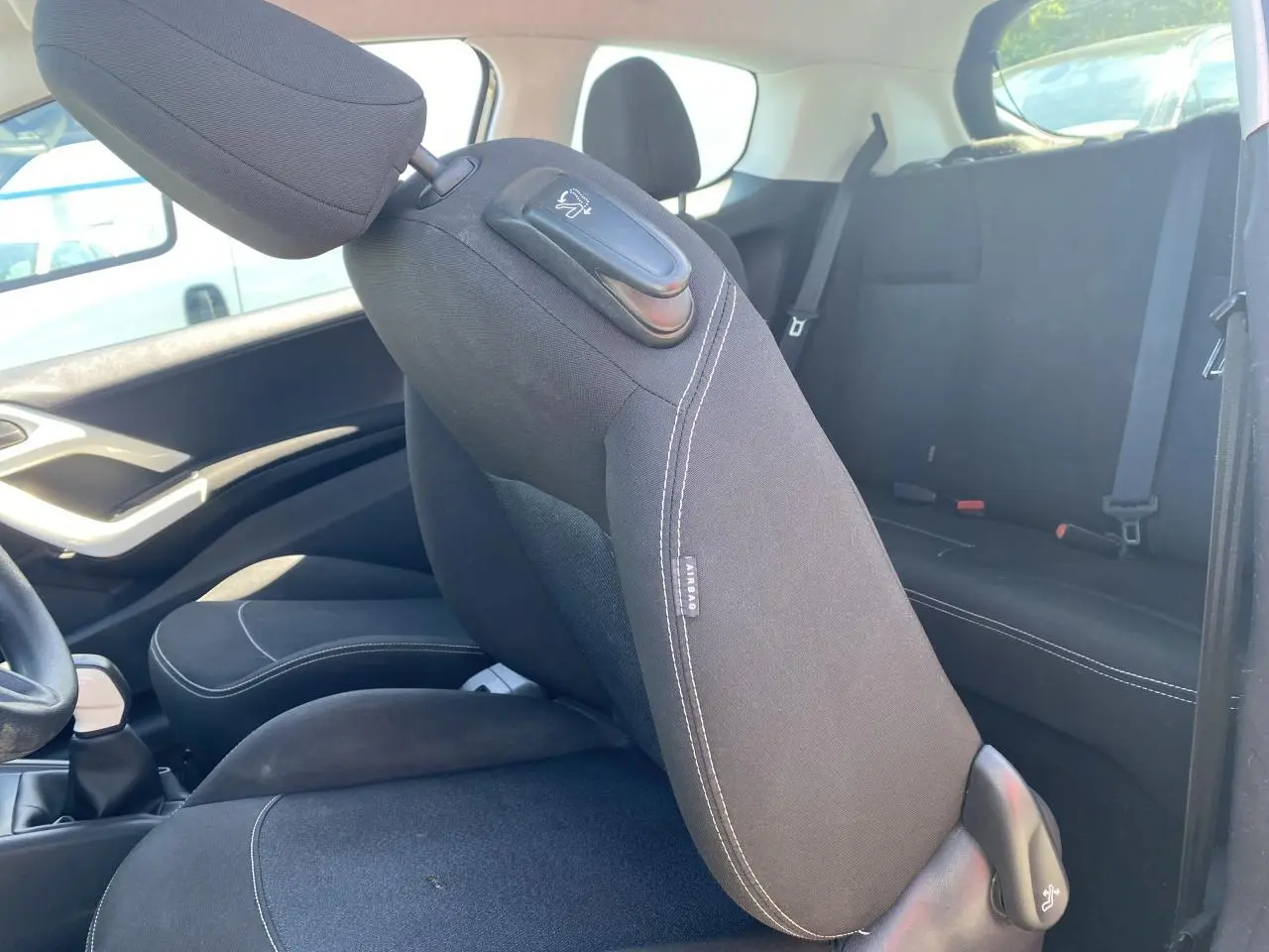 Vue intérieure côté gauche de la Peugeot 208 2018, sièges tissu noir avec surpiqûres blanches et dossier avant rabattable.