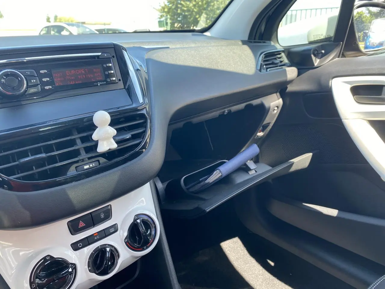 Vue intérieure côté passager de la Peugeot 208 gris foncé 2018, avec boîte à gants ouverte et tableau de bord blanc.
