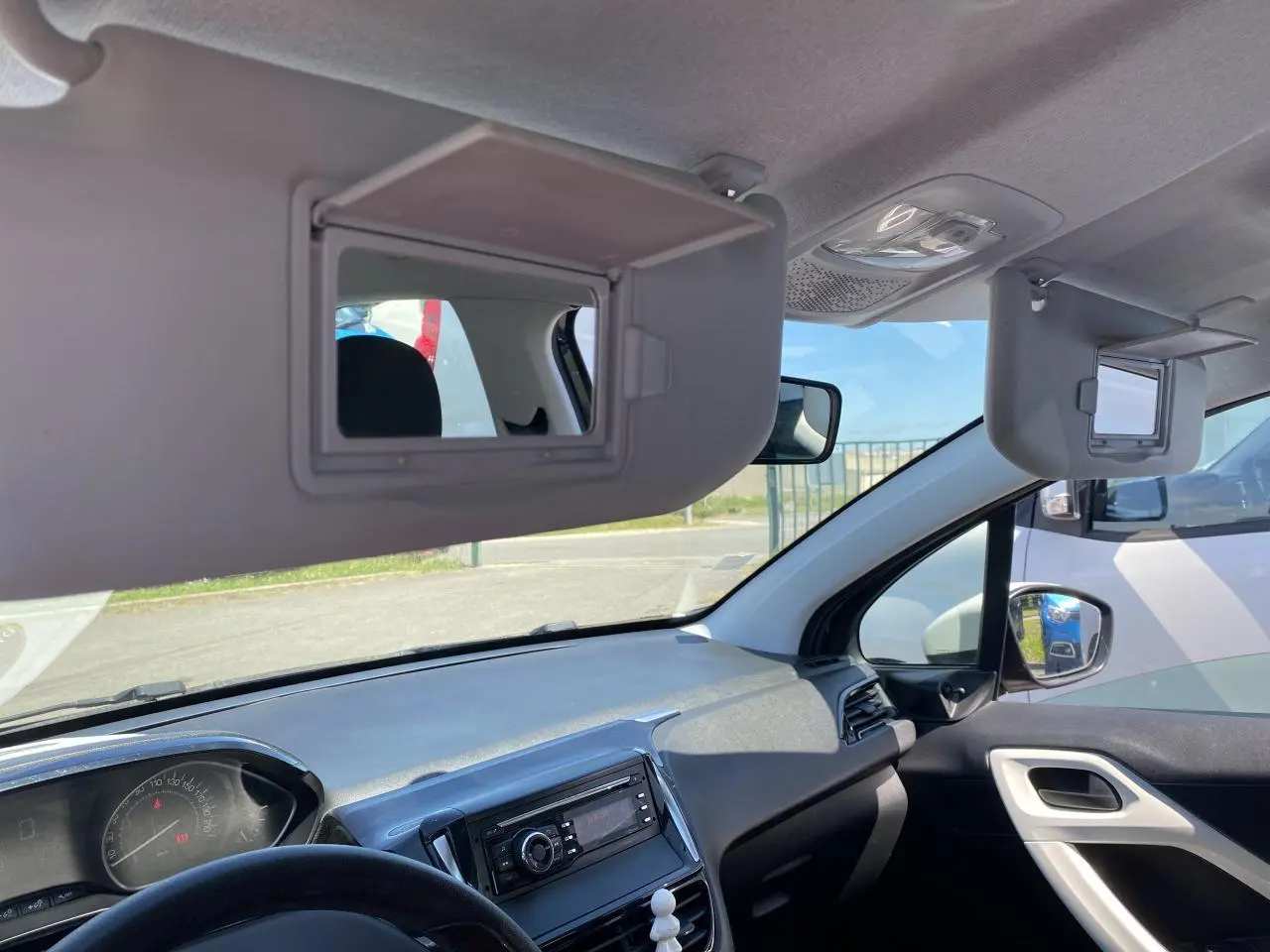 Intérieur Peugeot 208 2018 vu côté passager, tableau de bord gris avec pare-soleils ouverts et miroirs intégrés.