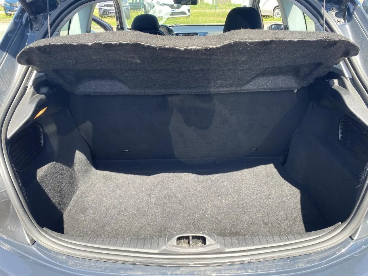 Coffre ouvert vu de l'arrière d'une Peugeot 208 gris foncé, montrant un espace de rangement propre et vide.