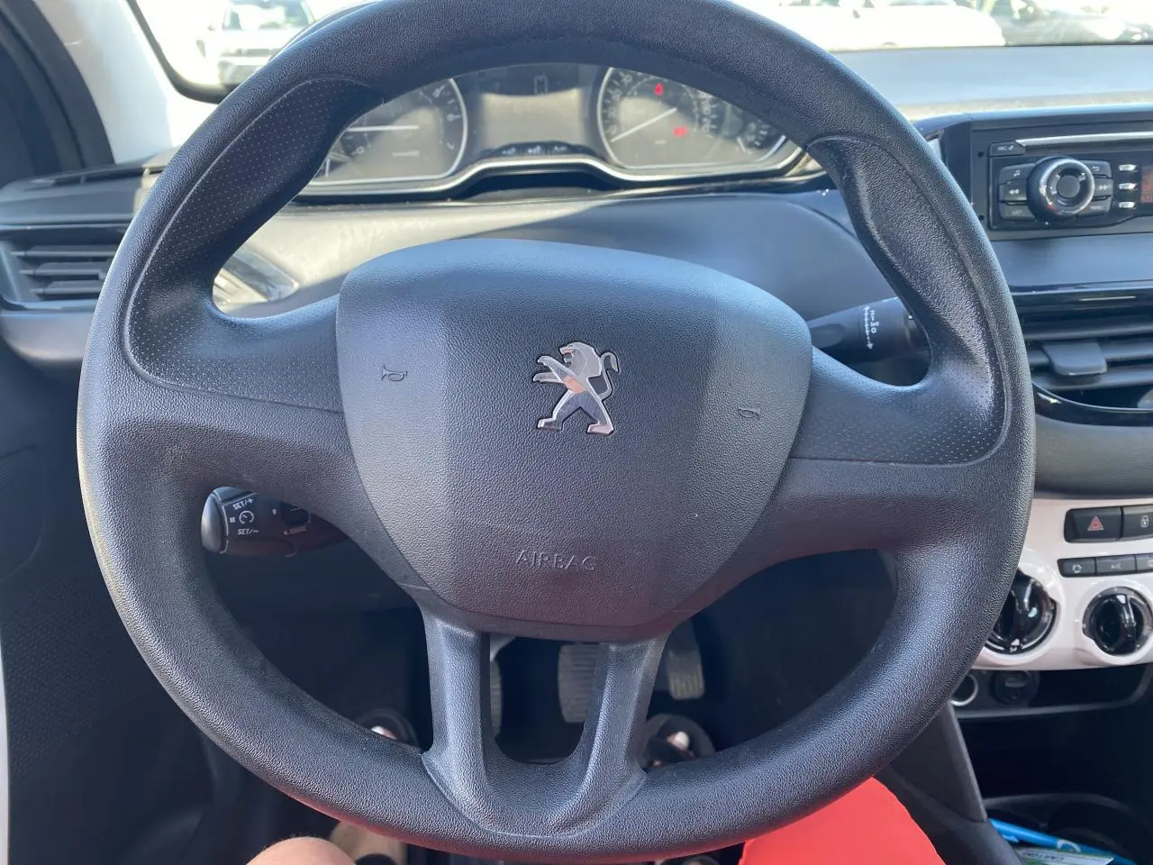 Vue rapprochée du volant noir avec logo Peugeot au centre, tableau de bord et console centrale en arrière-plan.
