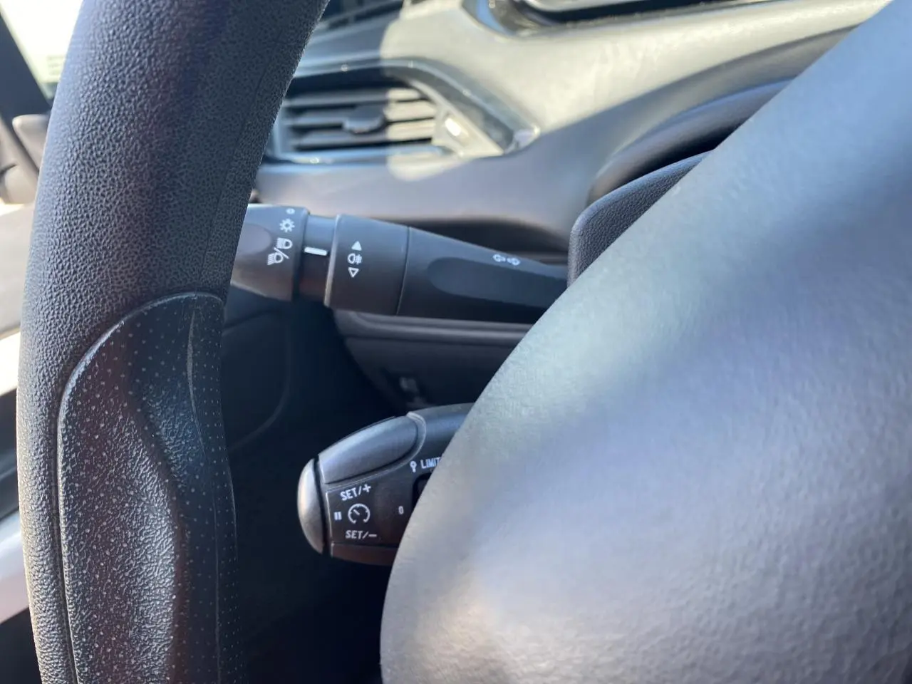 Gros plan sur le volant noir de la Peugeot 208 gris foncé, montrant les commandes du régulateur de vitesse côté gauche.