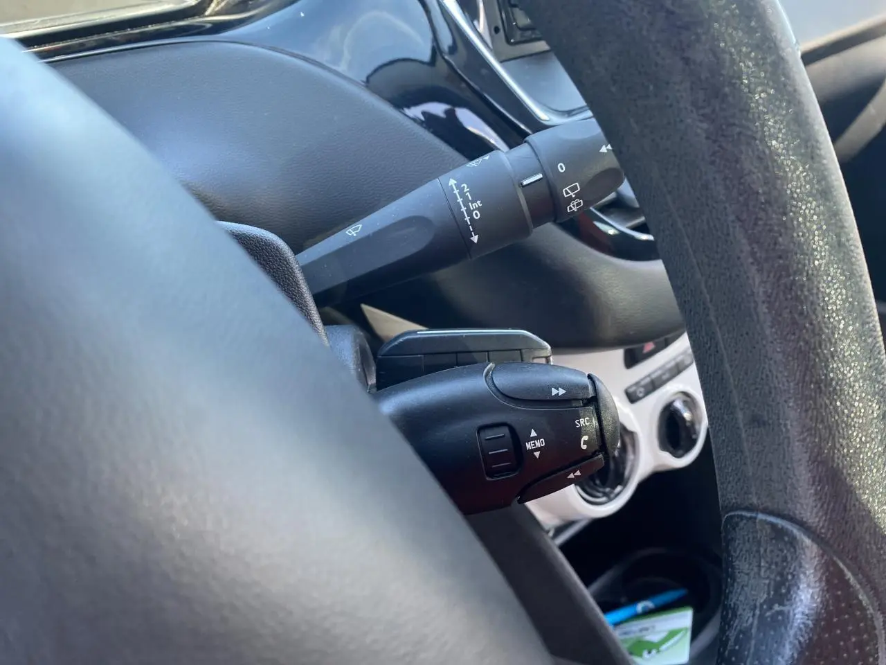 Gros plan sur la commande multifonction noire derrière le volant d’une Peugeot 208 gris foncé, intérieur épuré.