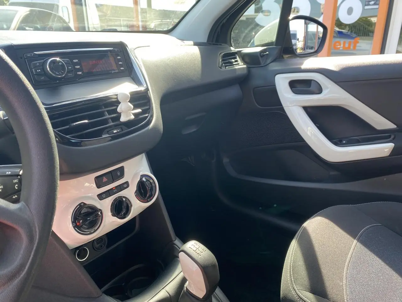 Vue intérieure côté passager de la Peugeot 208 2018, tableau de bord et console centrale avec détails blancs et levier de vitesse manuel.