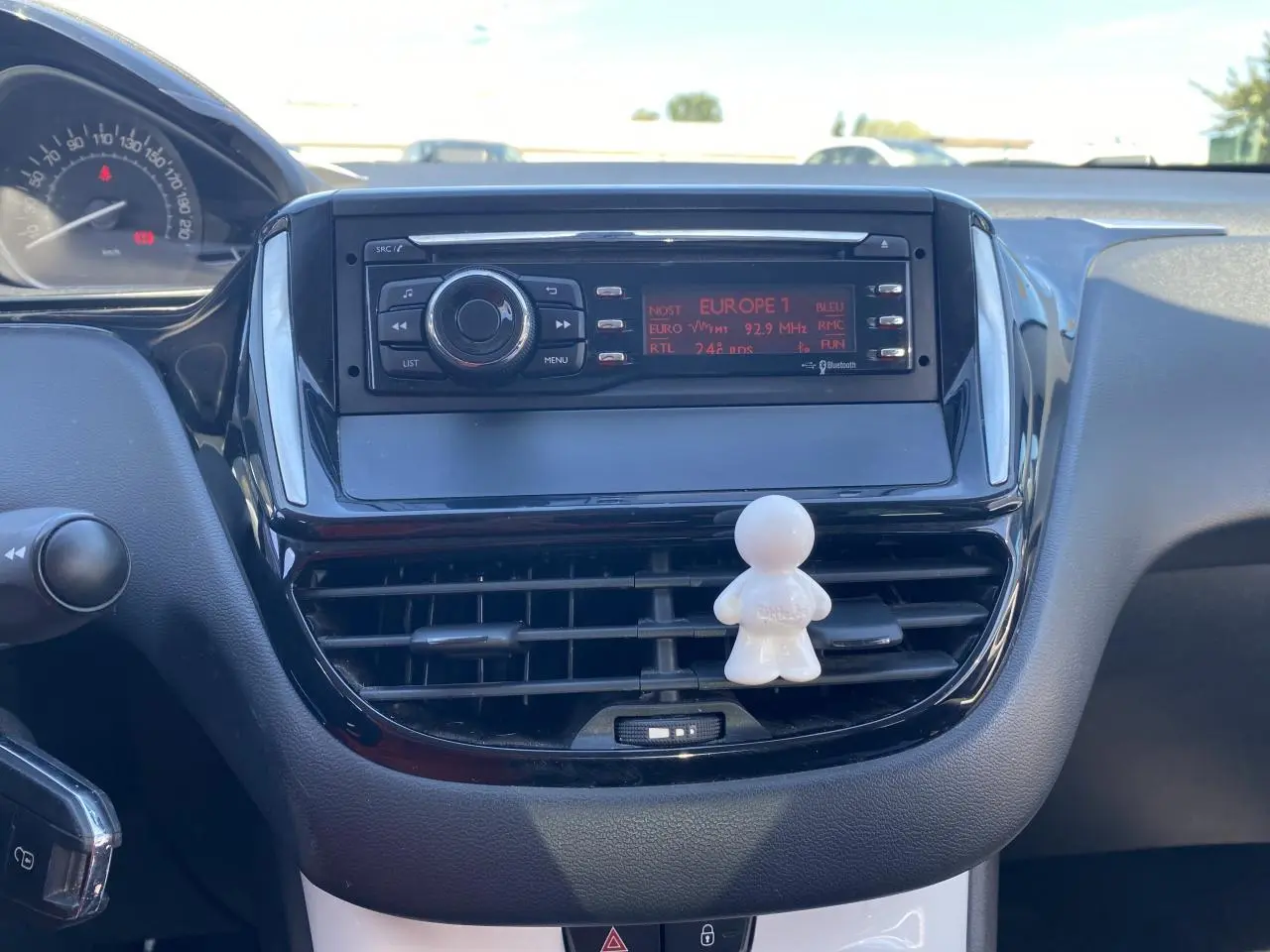 Vue rapprochée du tableau de bord de la Peugeot 208 gris foncé, avec autoradio et ventilation centrale décorée d’un petit personnage blanc.
