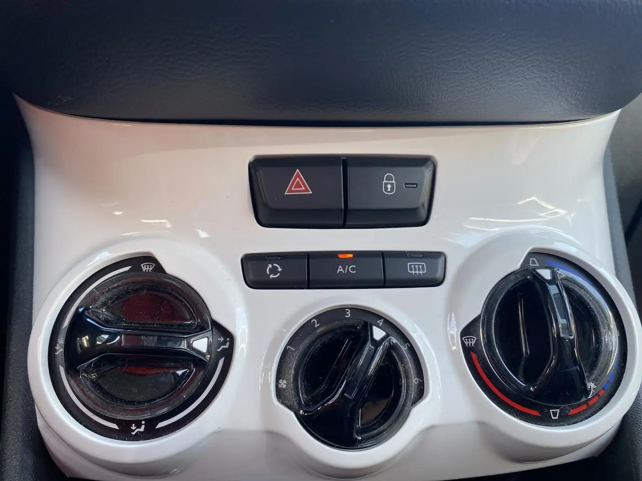 Gros plan sur la console centrale blanche du Peugeot 208 2018, avec commandes de climatisation et boutons de sécurité.