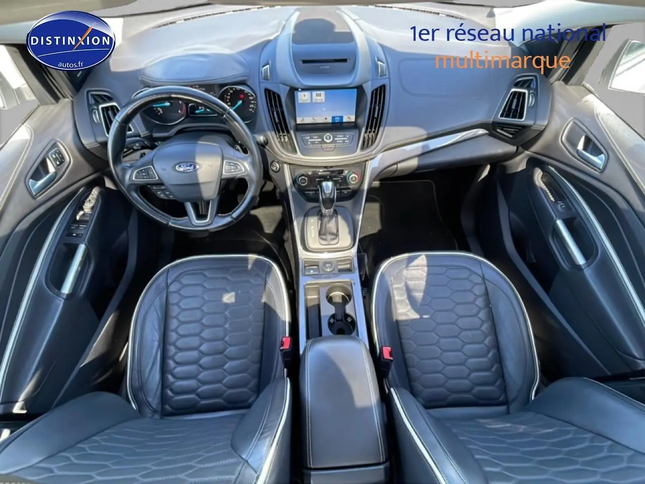 Vue intérieure de face du Ford Kuga 2017, sièges sport noirs en cuir et tableau de bord avec écran central tactile.