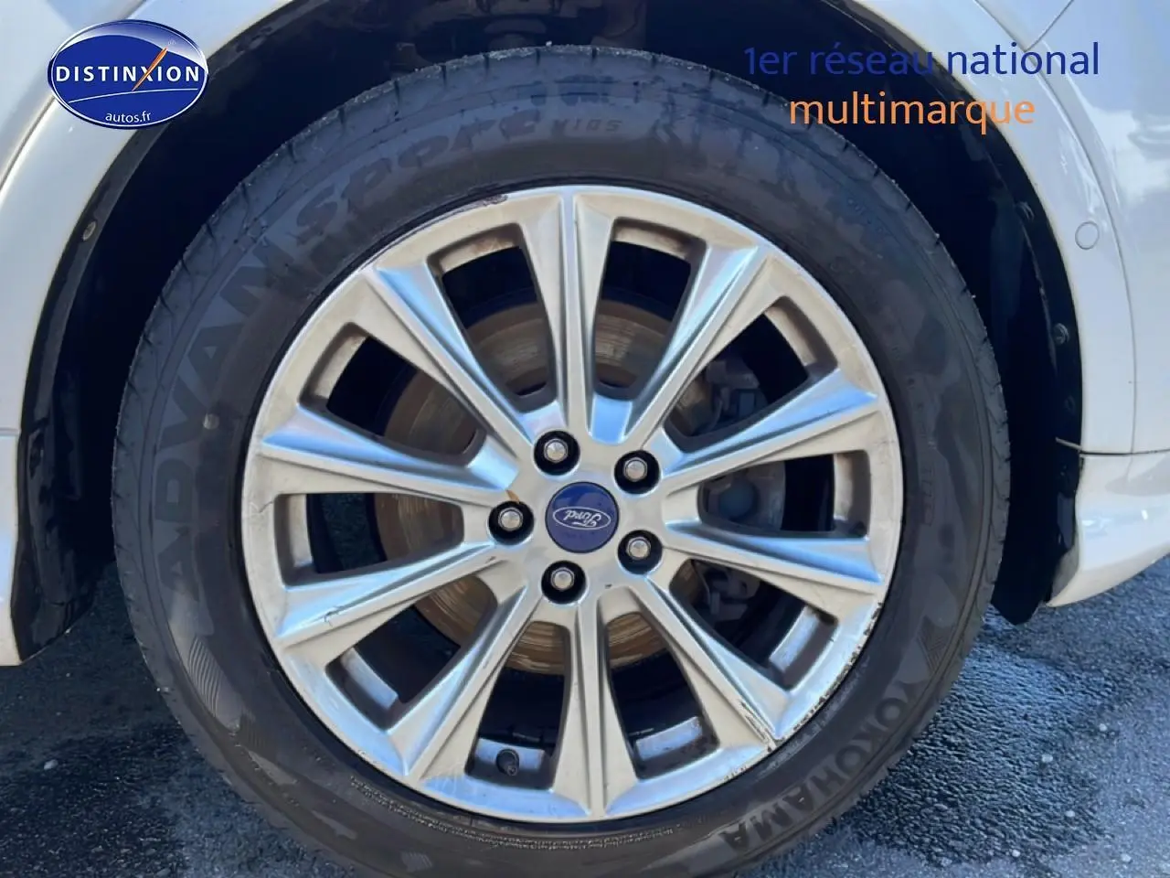 Gros plan sur la jante alu argentée avant droite du Ford Kuga blanc, avec logo Ford visible au centre.