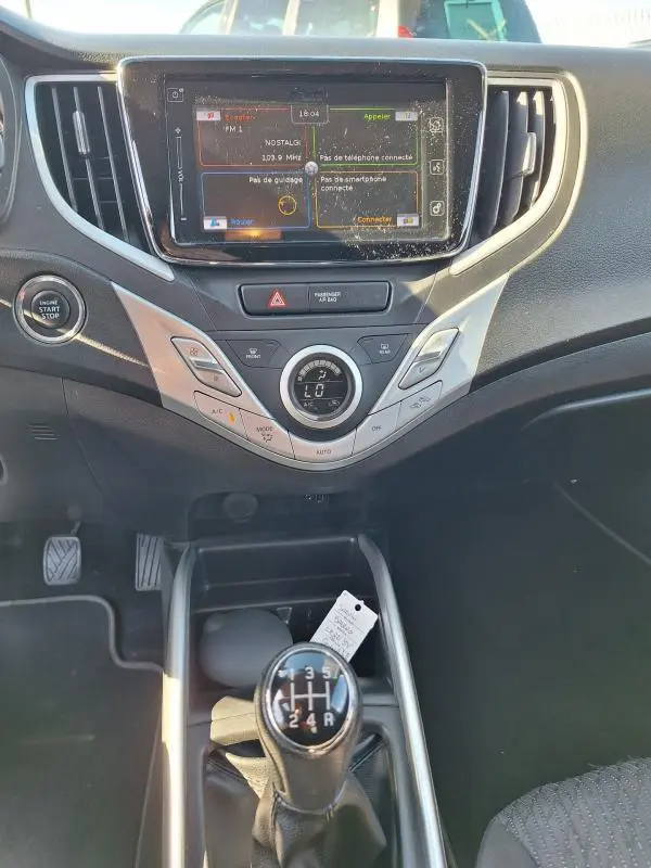 Vue intérieure centrée sur la console centrale et levier de vitesses manuelle d'une Suzuki Baleno gris clair de 2017.