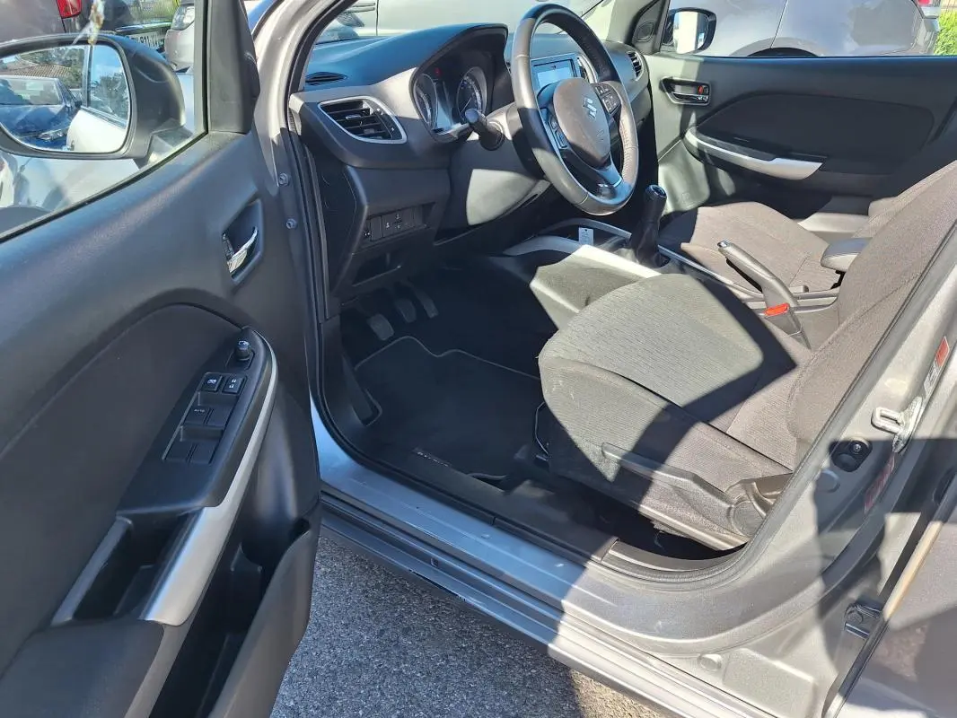 Intérieur côté conducteur de la Suzuki Baleno gris clair 2017, montrant le volant, la boîte manuelle et les sièges tissu.