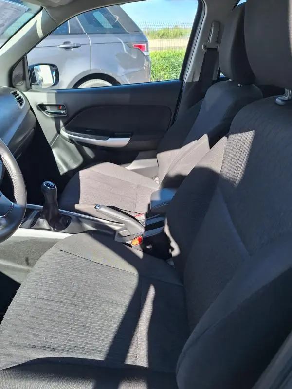 Vue intérieure côté conducteur de la Suzuki Baleno 1.0 Boosterjet Pack 2017, sièges tissu gris et levier de vitesses manuel visible.