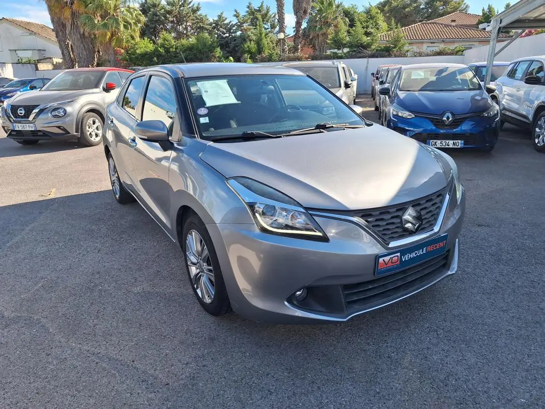 Vue 3/4 avant d'une Suzuki Baleno gris clair 2017 avec jantes alliage et phares xénon visibles.