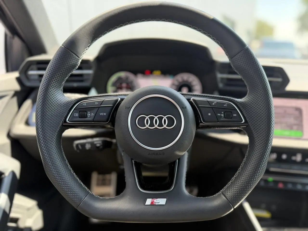 Volant cuir sport multifonctions Audi S-Line vu de face avec logo anneaux et commandes intégrées, intérieur noir.