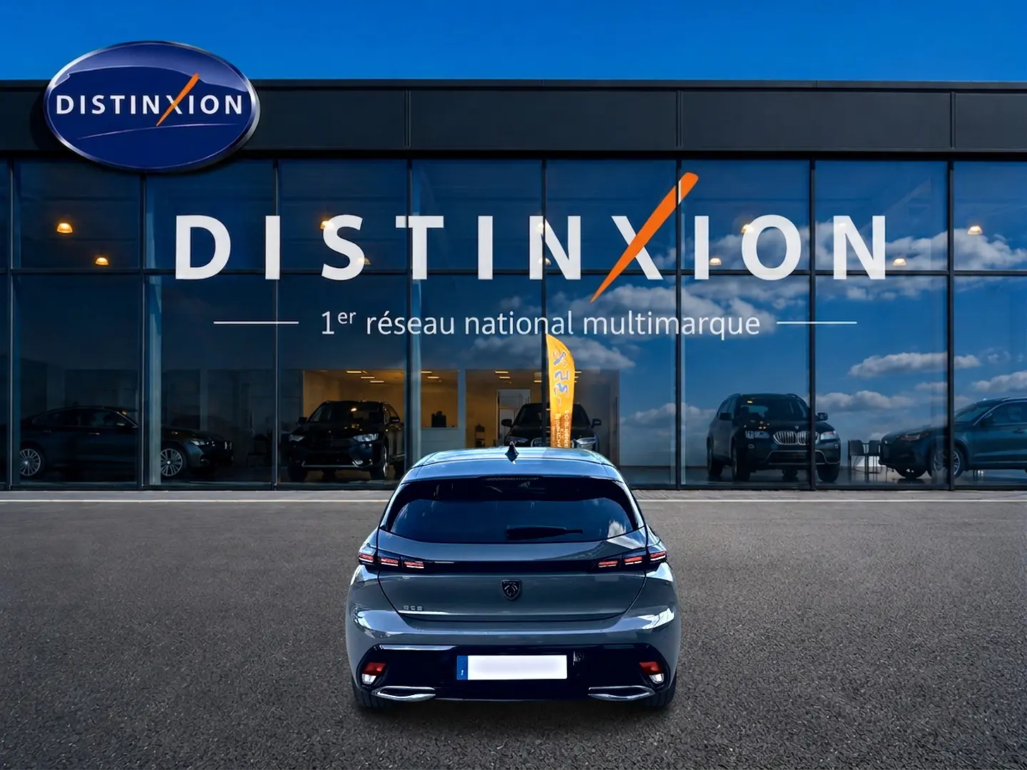 Vue arrière d'une Peugeot 308 gris selenium 2025 garée devant une vitrine avec logo Distinxion.