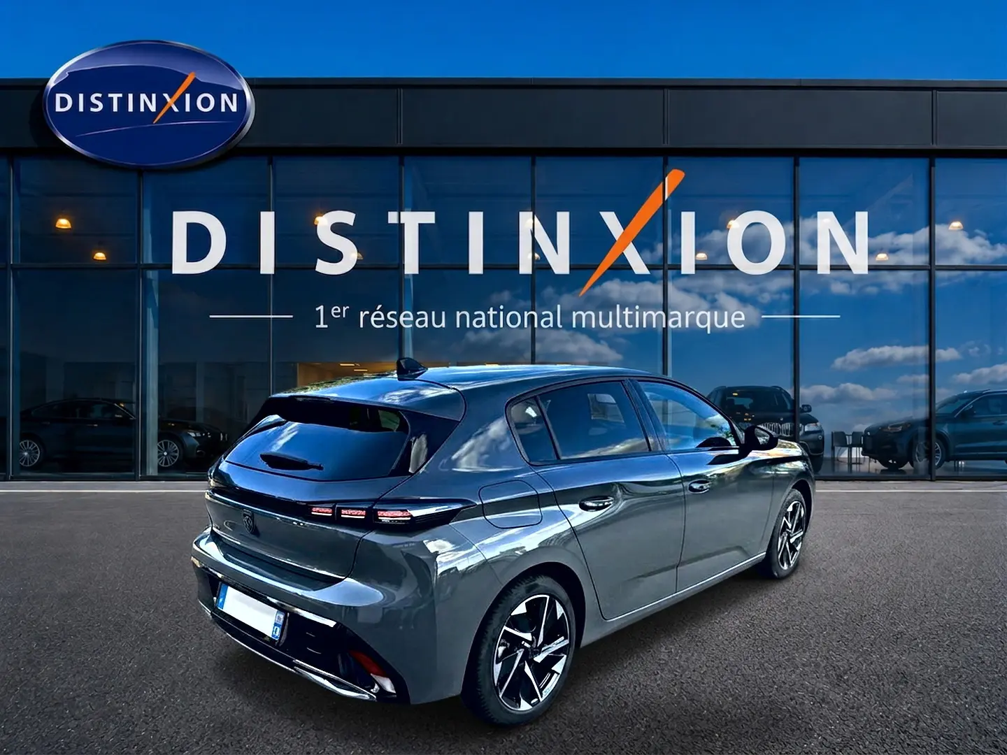 Vue 3/4 arrière droite d'une Peugeot 308 2025 gris selenium avec jantes alliage devant une vitrine Distinxion.