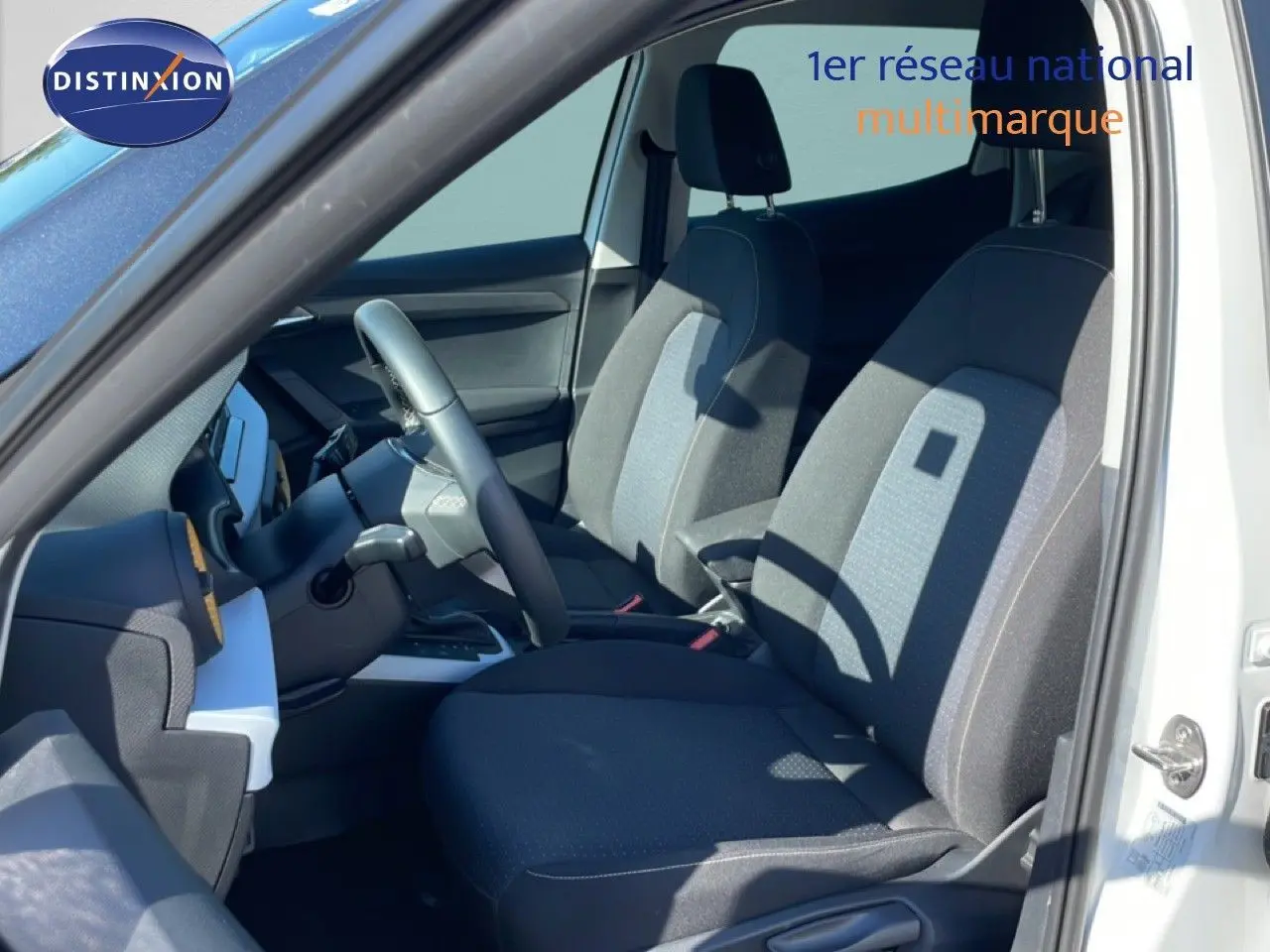 Vue intérieure côté conducteur du SEAT Arona blanc métal 2025, sièges tissu gris foncé avec inserts clairs.