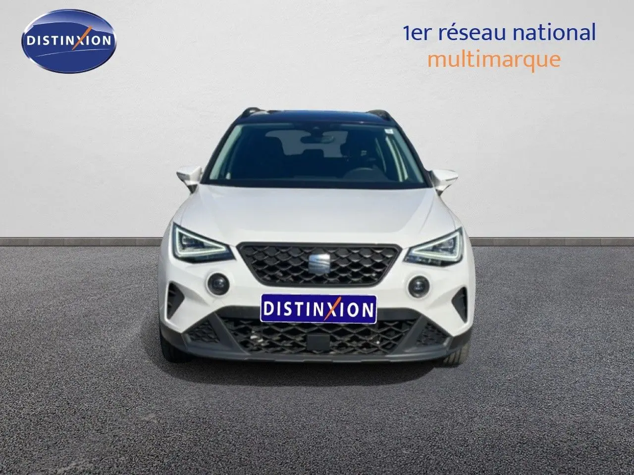 Vue frontale d'un SEAT Arona blanc métal avec toit noir, calandre noire et feux LED anguleux visibles.