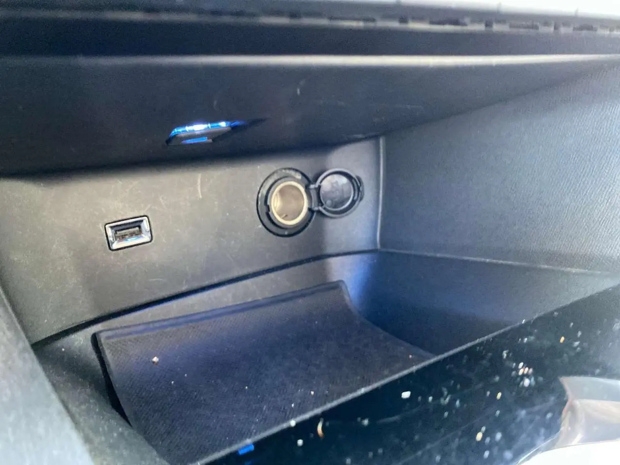 Prise allume-cigare et port USB dans le rangement central d'un Peugeot 3008 2019, intérieur noir.