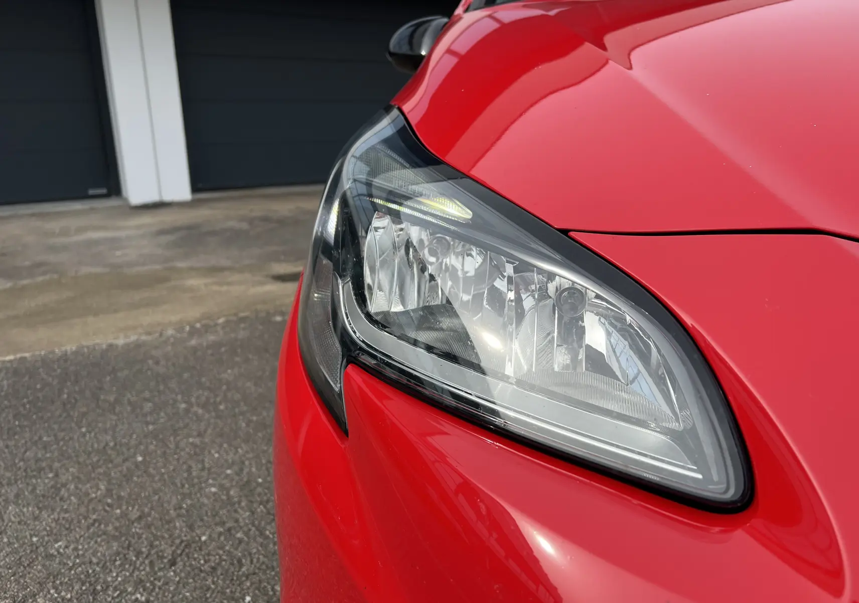 Gros plan sur le phare avant gauche de l'Opel Corsa rouge avec toit noir brillant, soulignant son design moderne.