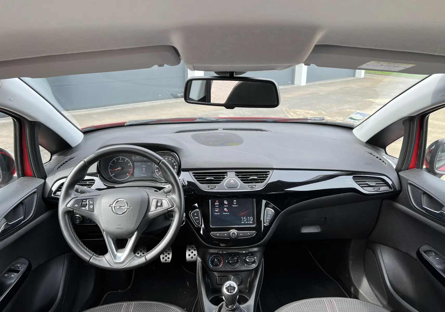 Vue intérieure avant de l'Opel Corsa rouge avec tableau de bord noir brillant et volant multifonctions cuir.