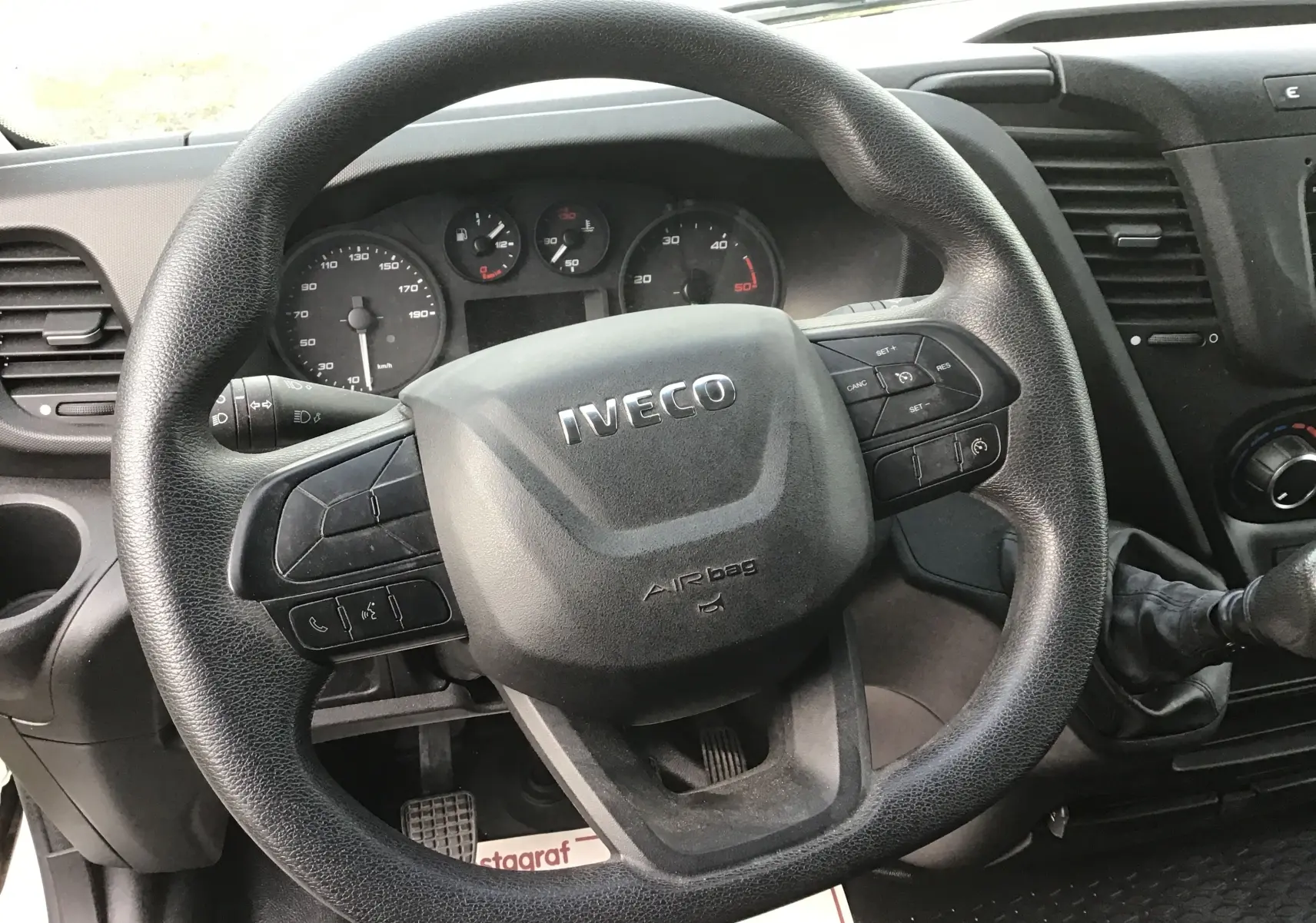 Vue rapprochée du volant noir d’un Iveco Daily Fourgon 2023 avec tableau de bord et levier de vitesses manuelle visibles.