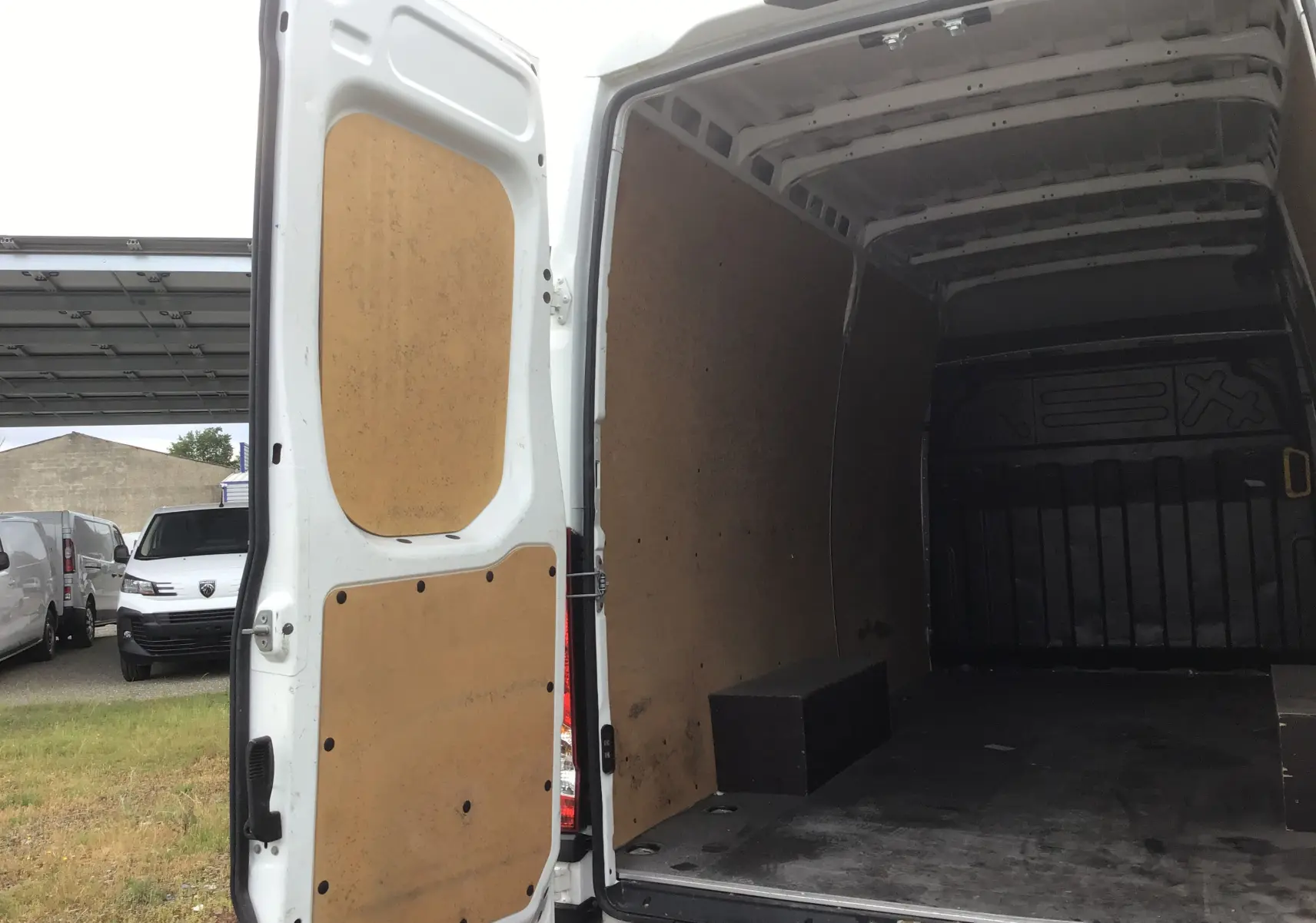 Vue arrière ouverte du fourgon Iveco Daily blanc 2023, montrant l’intérieur cloisonné avec revêtement bois.
