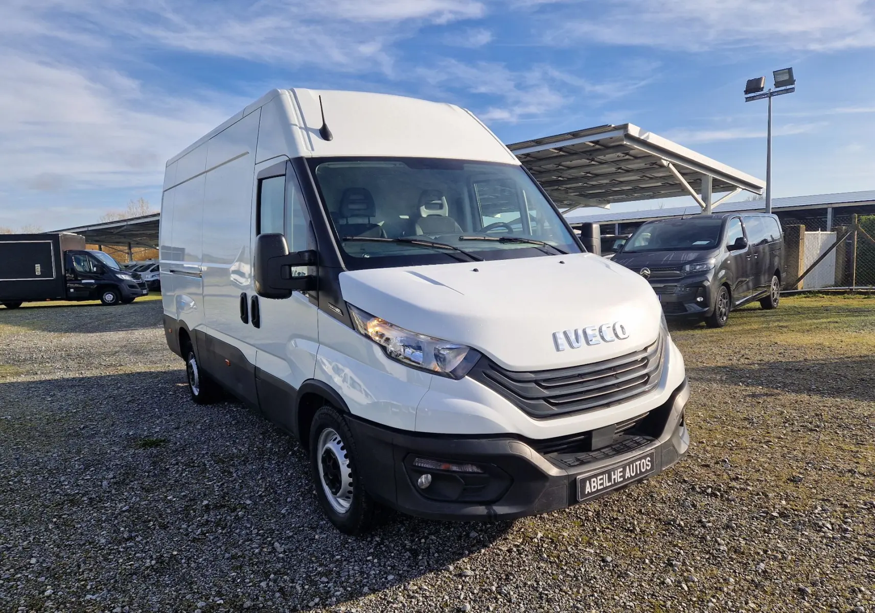Fourgon Iveco Daily blanc vu en 3/4 avant droit sur un parking extérieur avec ciel bleu.