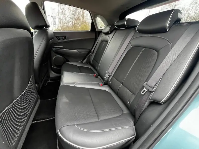 Vue intérieure côté droit de la banquette arrière en cuir noir du Hyundai Kona bleu, avec ceintures de sécurité visibles.