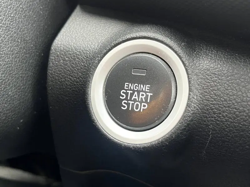 Gros plan sur le bouton noir de démarrage moteur entouré d'un anneau argenté dans l'habitacle d'une Hyundai Kona bleu.