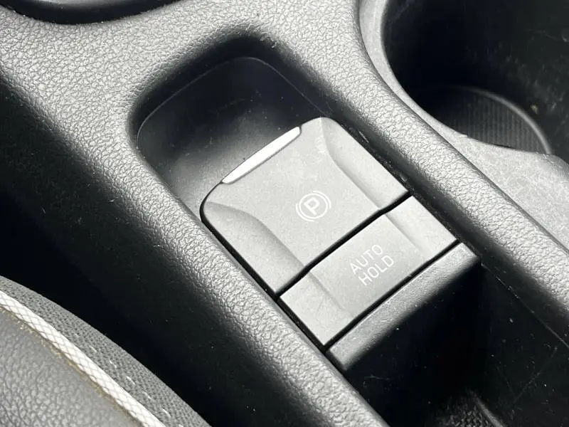 Gros plan sur la commande de frein à main électronique et bouton Auto Hold dans l'habitacle noir du Hyundai Kona bleu.