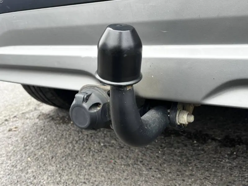 Gros plan sur l'attelage de remorque noir sous le pare-chocs arrière gris d'un Hyundai Kona hybride.