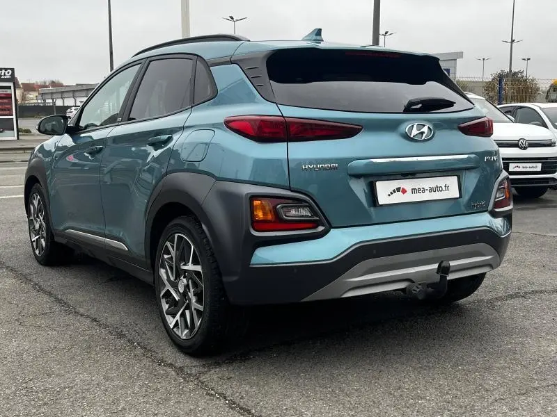 Vue 3/4 arrière droite d'un Hyundai Kona bleu avec jantes alu et hayon teinté sur parking urbain.