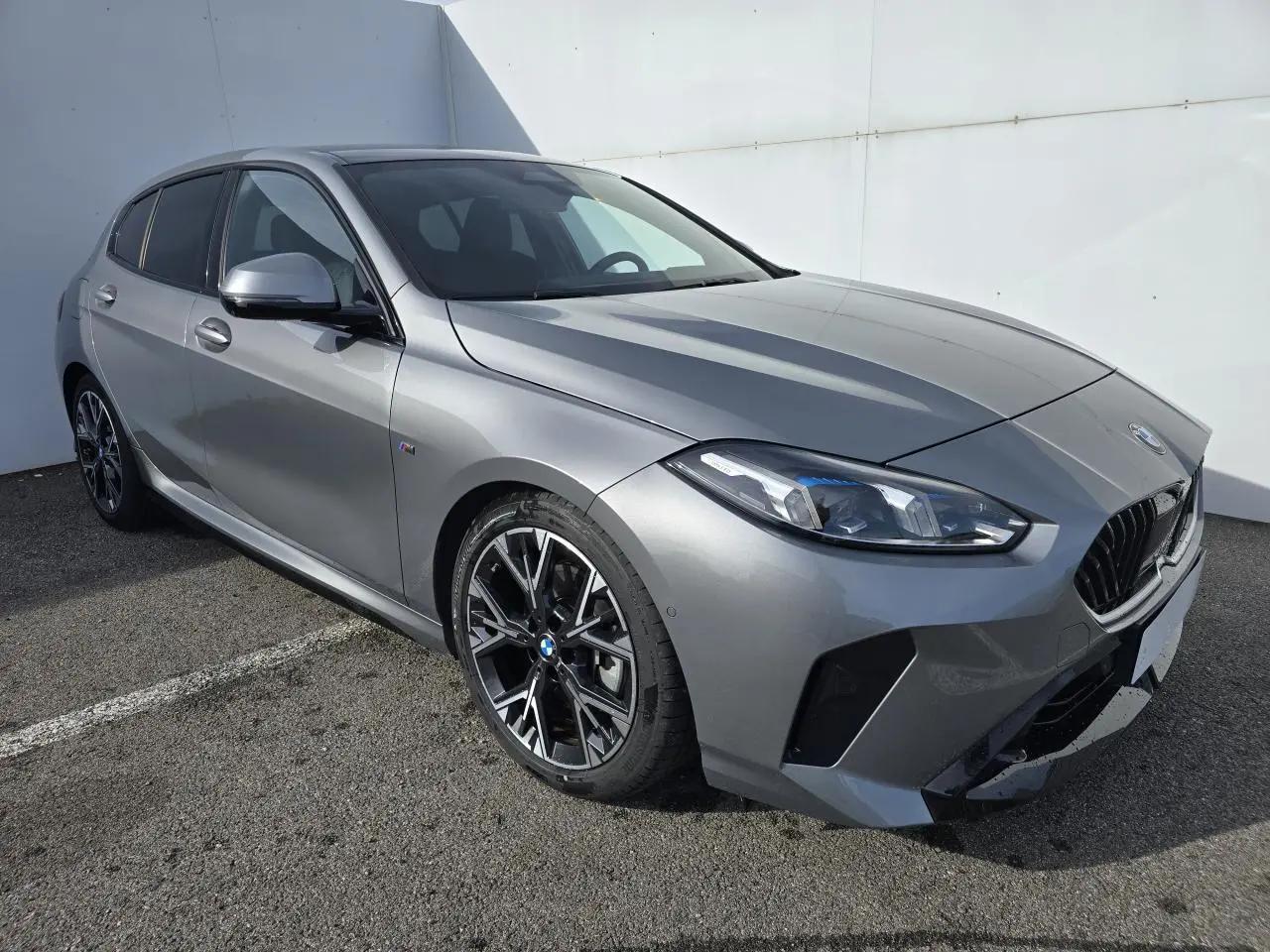 BMW Série 1 gris Skyscraper vue 3/4 avant droit avec calandre noire et jantes alliage 18 pouces M Sport.